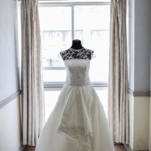 A beautifully crafted white bridal gown displayed on a mannequin in a softly lit room.